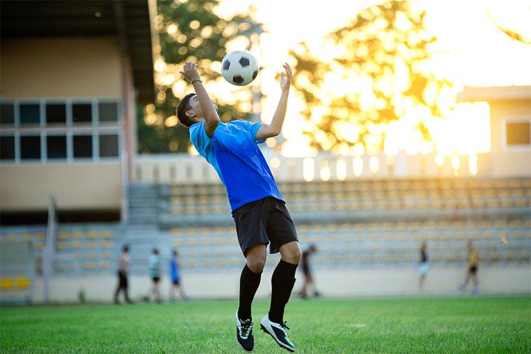 A boy plays with a ball in the air which is a part of becoming a professional soccer player