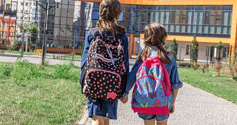 Two young girls with backpacks are going to school