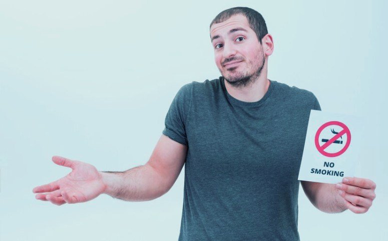 A man is holding a piece of paper that says no smoking