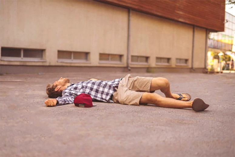 A man in a shirt and a red hat is lying on the road