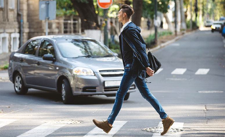 A man is crossing a crosswalk and a car is approaching him