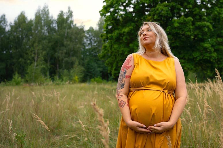 A pregnant women with yellow dress walk into the woods