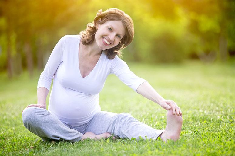 A smiling woman who is pregnant doing streching