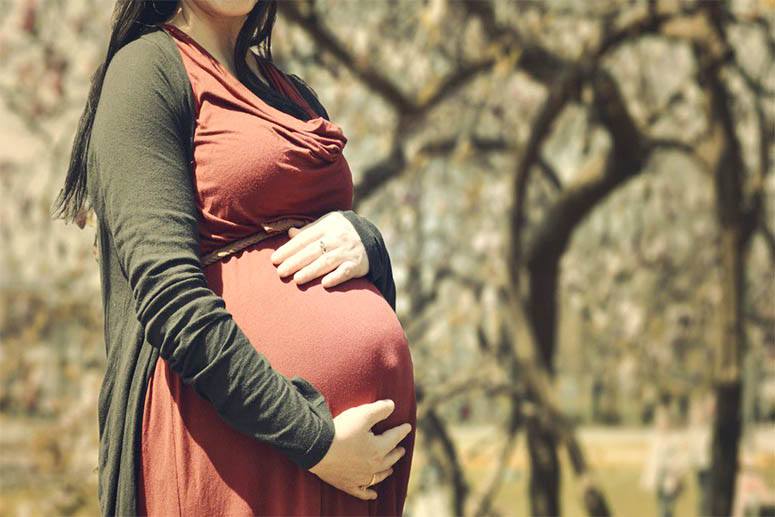 Pregnant woman holding her stomach in the nature