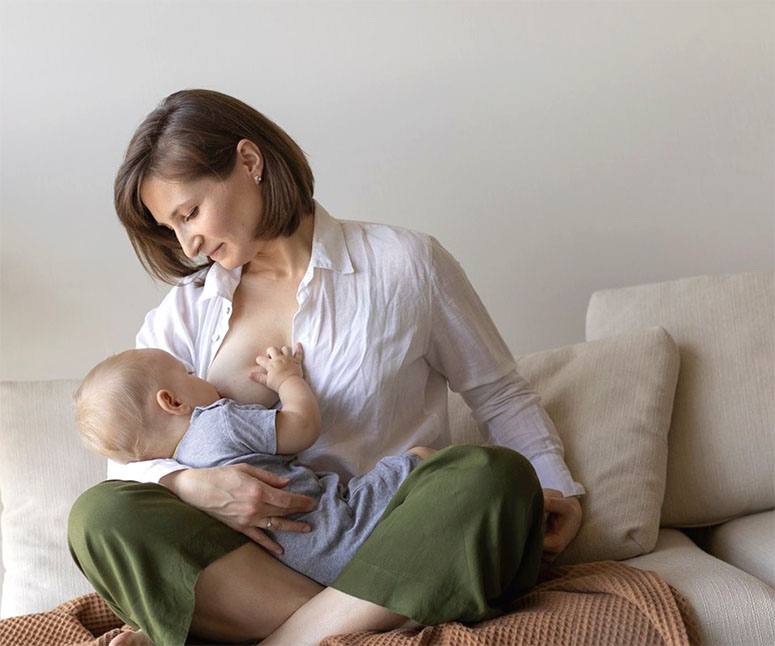 An elderly mother is nursing her child on the sofa and looking at him