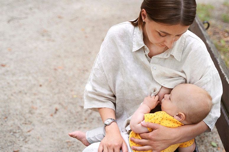 A mother breastfeeds her baby outside on a bench