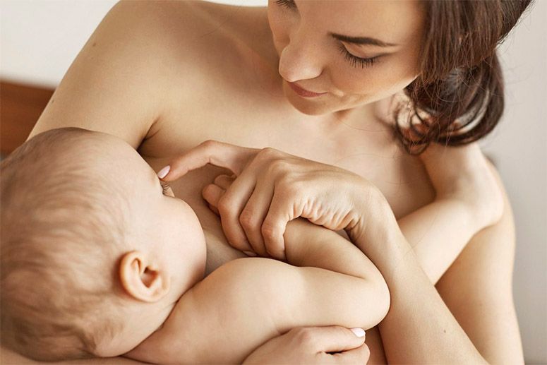 A young naked girl breastfeeding her baby