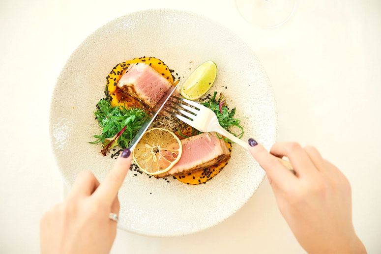 Woman's hands is holding cutlery over a salmon dish