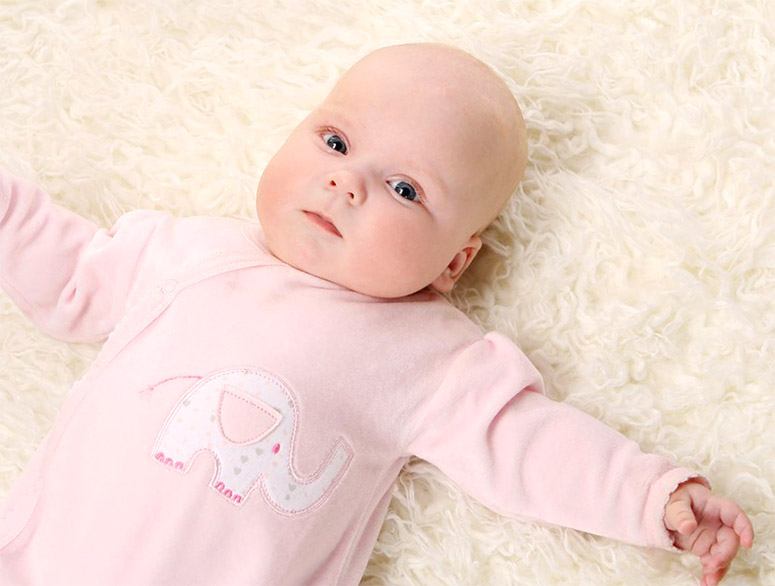 Baby in pink dress laying on a bed