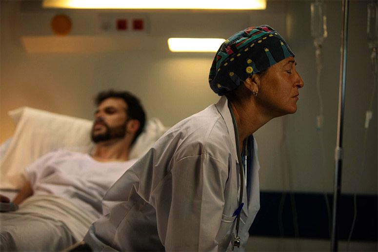 A desperate woman sits next to her son in a hospital bed