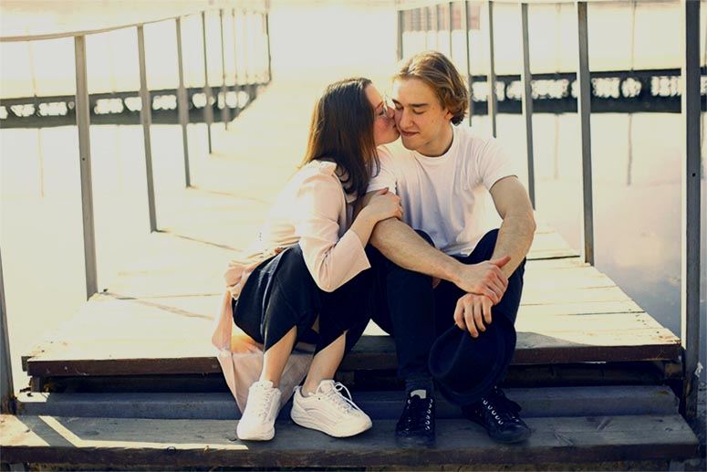 A woman kisses a boy by a bridge